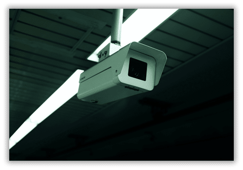 A low-angle shot of a white surveillance camera hanging from an industrial ceiling.